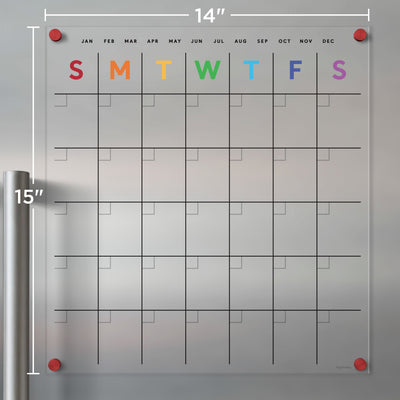 The Clear Acrylic Monthly Fridge Calendar | Rainbow Text by Girl Friday measures 14x15 inches and features rainbow-colored weekday letters. A monthly grid layout is secured in each corner with four sleek stainless steel magnets for a stylish finish.