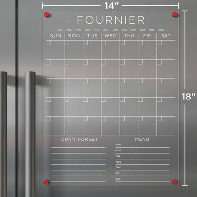 The Girl Friday Clear Acrylic Monthly Fridge Calendar (14x18 inches) features a customizable family name and bottom sections, a Sunday-to-Saturday grid for notes and menus, red magnets for easy attachment to metallic surfaces, and includes wet-erase markers.