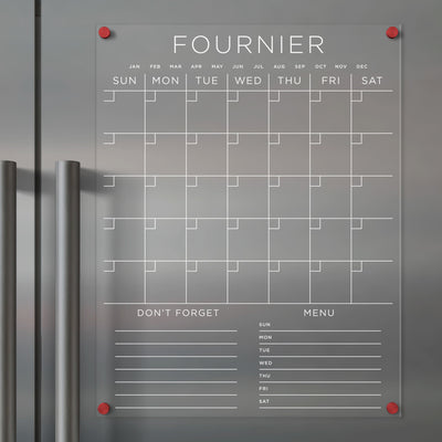 The Girl Friday Clear Acrylic Monthly Fridge Calendar boasts a weekly grid layout, sections for months, weekdays, Dont Forget, and Menu. Use wet-erase markers on its magnetic surface with red corner magnets for style and stability. Personalize with your family name in white text.