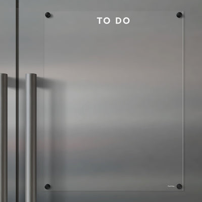 The Girl Friday Clear Acrylic Fridge To Do List features white text and mounts on metallic surfaces. It has two vertical metal handles on the left, perfect for quick updates with wet-erase markers.