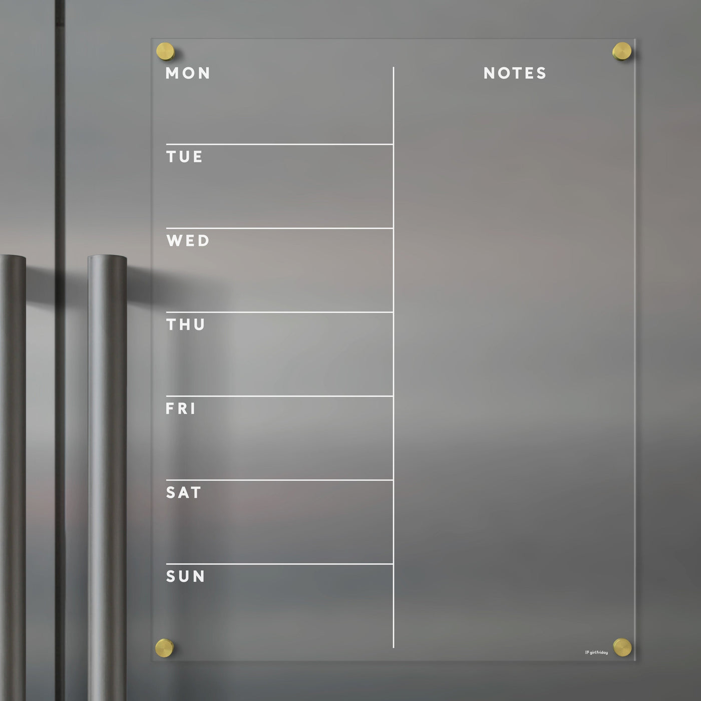 The Girl Friday Clear Acrylic Fridge Calendar is a minimalistic glass weekly planner featuring Mon to Sun columns and Notes. It includes gold corner pegs, two gray handles on the left, and is compatible with wet-erase markers for easy updates.