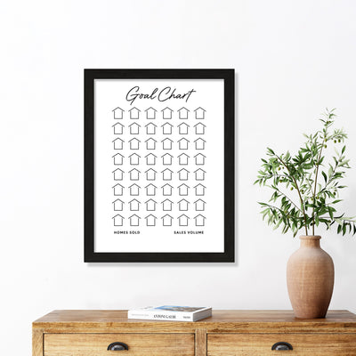 Girl Friday Shops Goal Chart | Sales Tracker for Real Estate elegantly tracks homes sold and sales volume with customizable house icons, beautifully displayed above a wooden table adorned with stacked books and a potted plant in a beige vase.