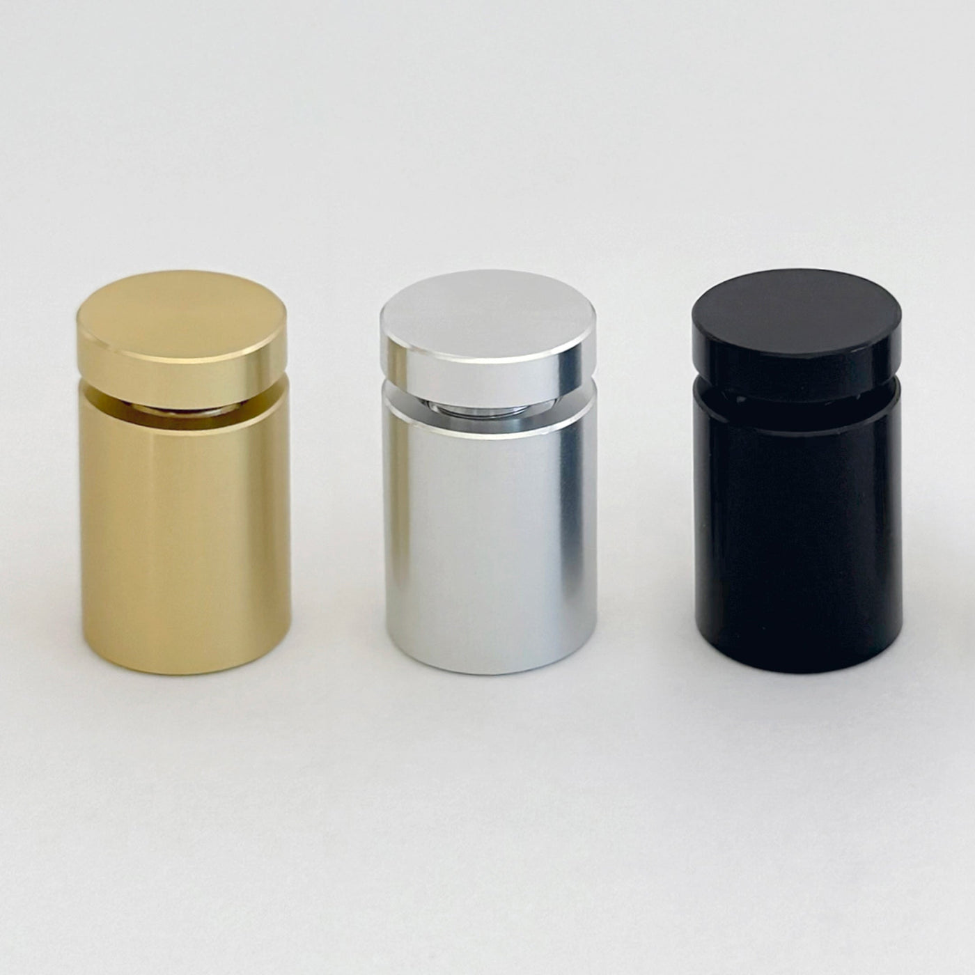 Three sleek, shiny Toilet Acrylic Signs by Girl Friday Shop stand in a row against a white background, featuring smooth surfaces and custom cylindrical designs. They are colored gold, silver, and black from left to right.