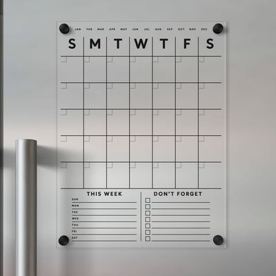 The Clear Acrylic Fridge Calendar by Girl Friday Shop is a minimalist, magnet-mounted acrylic calendar for your fridge. It features black text with a grid layout, days of the week, This Week and Dont Forget sections, plus lines and checkboxes for customization with wet-erase markers.