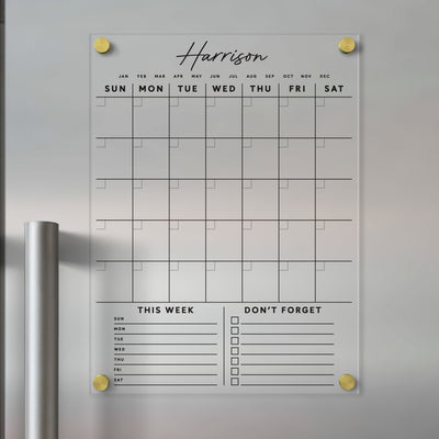 The Clear Acrylic Monthly Fridge Calendar from Girl Friday helps organize busy days with customizable family names and bottom sections. It features daily spaces, This Week, and Dont Forget checkboxes, all writable with dry-erase markers and enhanced by elegant black text.