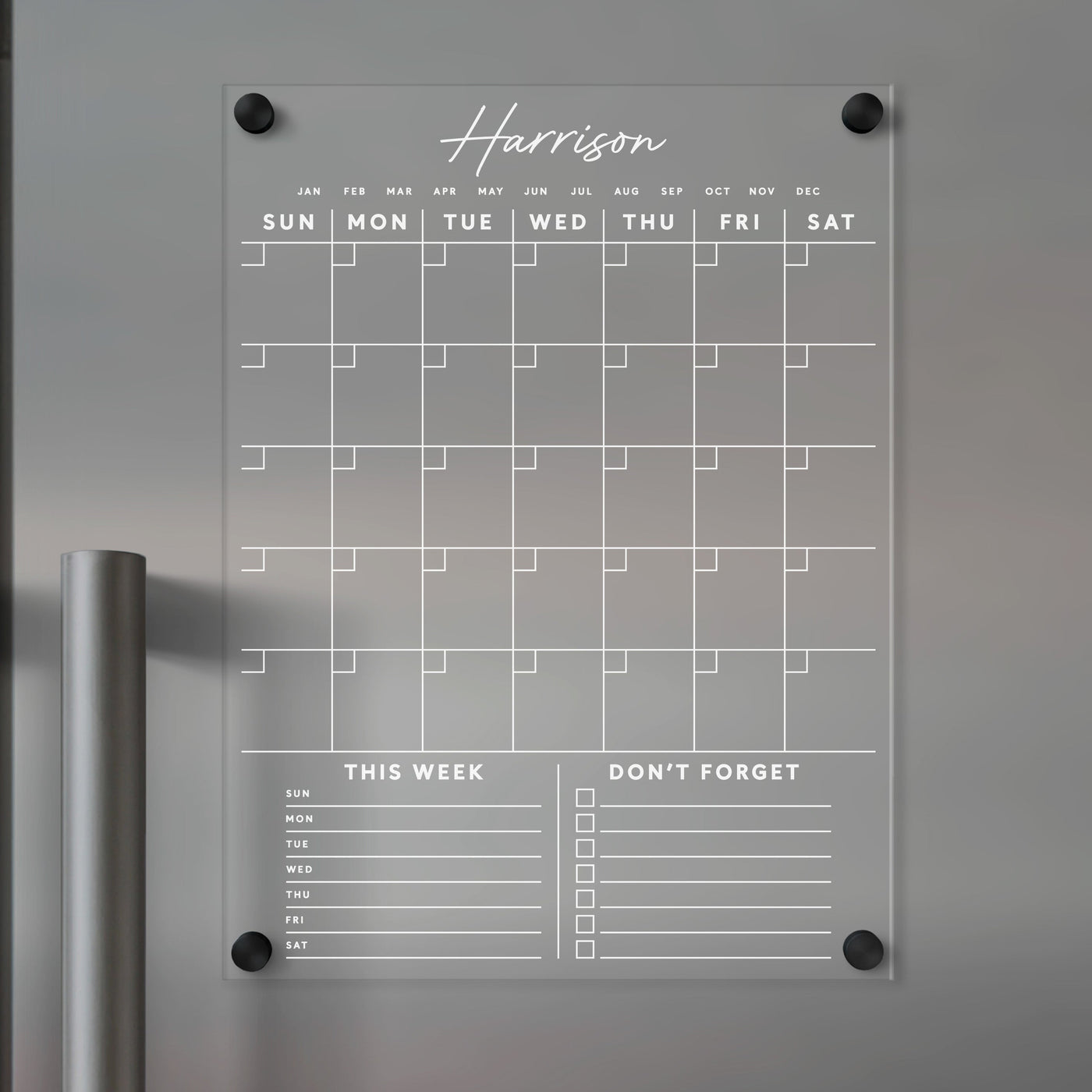 The Clear Acrylic Monthly Fridge Calendar from Girl Friday features an elegant monthly grid for daily entries. It includes customizable This Week and Dont Forget sections at the bottom, ideal for wet-erase markers, and personalization with your family name in white text.