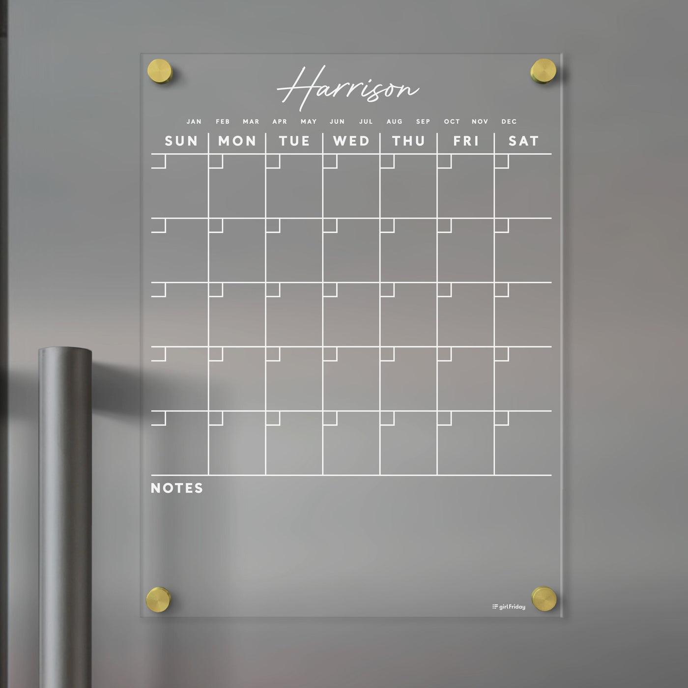 The Clear Acrylic Monthly Fridge Calendar by Girl Friday features a minimalist design with white outlines for wet-erase markers. Harrison is custom at the top, NOTES at the bottom, and gold fasteners in each corner. It showcases days of the week with large date squares.