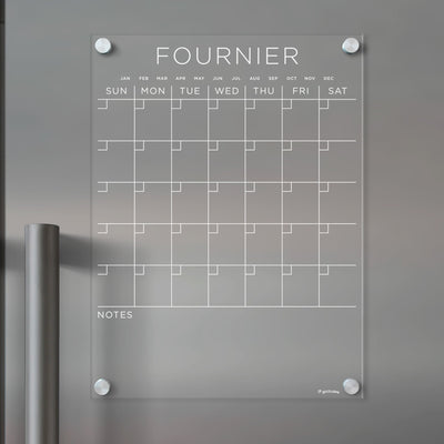The Girl Friday Acrylic Fridge Calendar, customizable with your family name, features a weekly grid and note sections for wet-erase markers. Mounted with four silver pegs, its designed to keep your family stylishly organized.