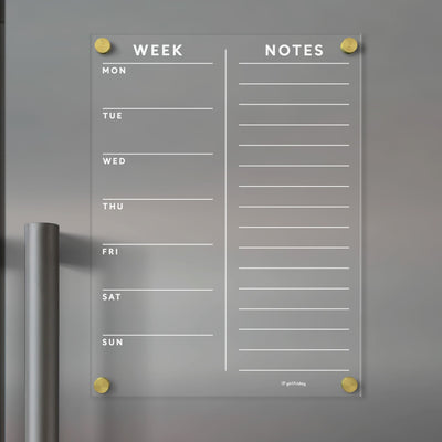 The Clear Acrylic Customizable Fridge Calendar by Girl Friday features Week columns from Monday to Sunday and a Notes section. Use wet-erase markers on its wall-mounted design with gold corners, adapting it seamlessly as a dynamic planner board.