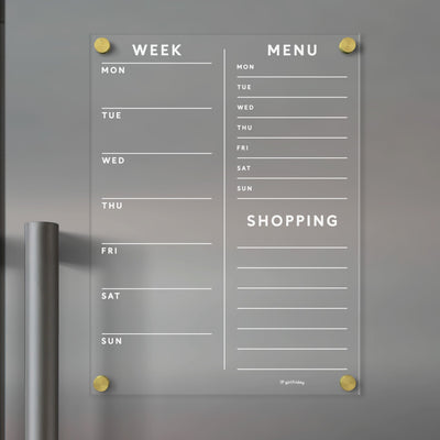 The Girl Friday Acrylic Fridge Planner is a customizable, wall-mounted acrylic planner featuring Week, Menu, and Shopping sections with days of the week. It uses gold pegs for mounting, making it perfect for dry-erase markers.