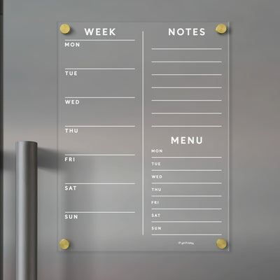 The Girl Friday Acrylic Fridge Planner displays sections for Week, Notes, and Menu with lined days from Monday to Sunday. Its mounted with gold-colored screws and can be customized using dry-erase markers.