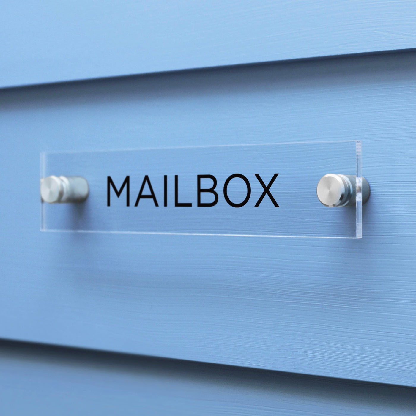 A custom-designed Mailbox Acrylic sign by Girl Friday Shop features MAILBOX in black letters on a sleek surface, mounted on a light blue wall with two chrome bolts.