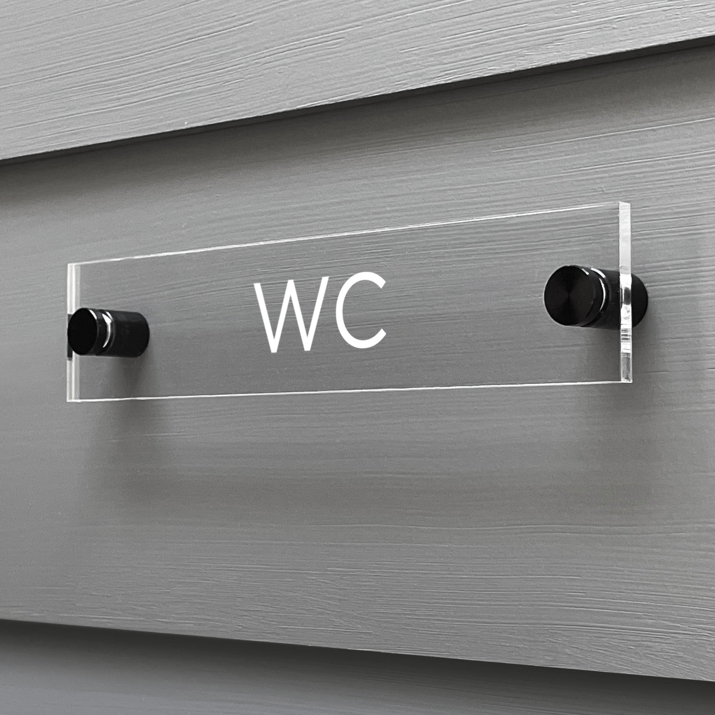 A custom-designed WC Acrylic Sign by Girl Friday Shop is mounted on a grey wall using sleek black standoffs.