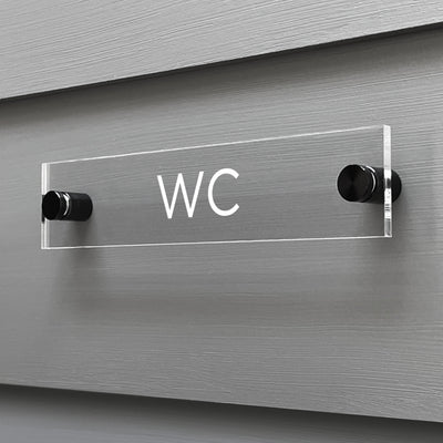 A custom-designed WC Acrylic Sign by Girl Friday Shop is mounted on a grey wall using sleek black standoffs.