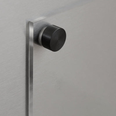 A black cylindrical wall bumper protects surfaces from door impact on a sleek metal wall, similar to how the Girl Friday Clear Acrylic Fridge Planner with customizable title and black text organizes your schedule.