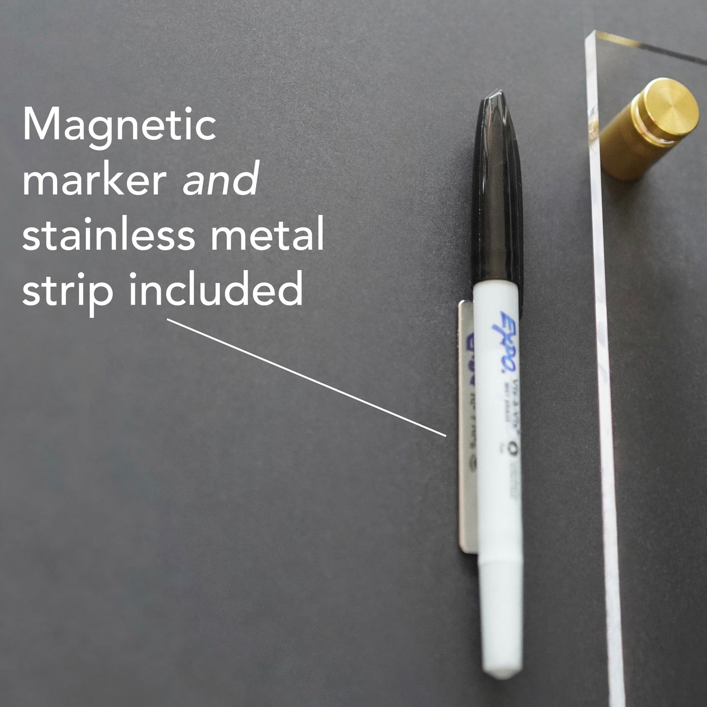A magnetic marker attaches to a stainless metal strip on a dark surface with polished edges. The text reads, Magnetic marker and stainless metal strip included, pointing to the marker. It pairs perfectly with the Girl Friday Shops Acrylic Calendar with bottom notes for seamless planning.