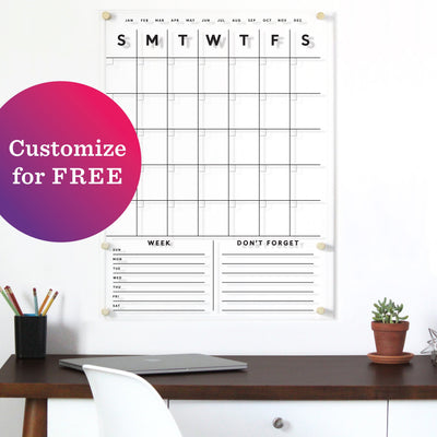 Above the wooden desk with a white chair is a Girl Friday Shop Acrylic Calendar with customizable options. A purple and pink gradient sticker says, Customize for FREE. On the desk are pencils, a plant, and a binder.