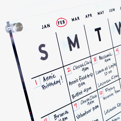 The Acrylic Calendar with bottom notes by Girl Friday Shop showcases February starting on a Thursday. Personal touches like handwritten Annies Birthday and club meetings enhance it, while February is highlighted with a red circle on this professionally printed creation.