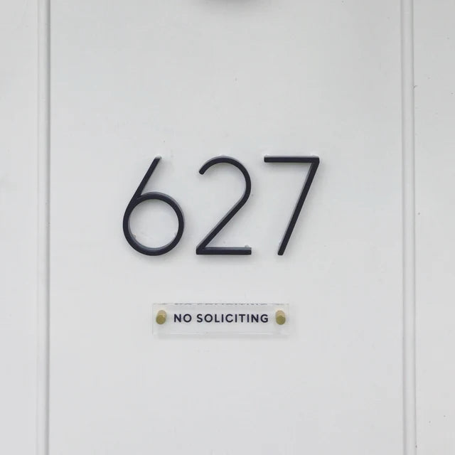 The image shows the number 627 in bold black digits on a white wall, with a Girl Friday Shops No Soliciting Acrylic sign in capital letters underneath.